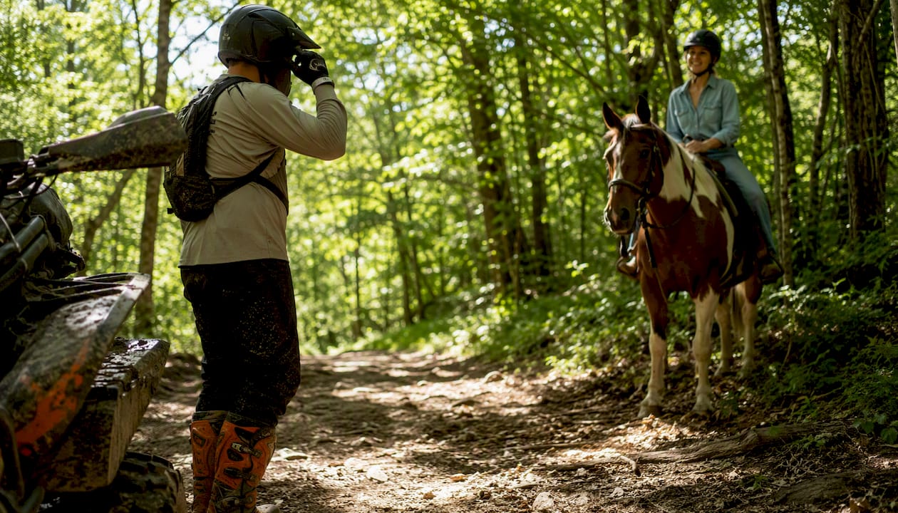 ATV rider removing helmet to yield to horse on trail