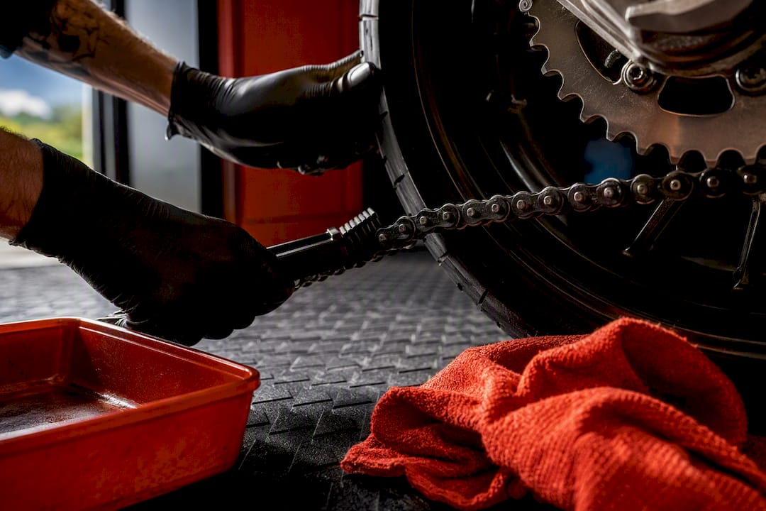 Hands cleaning a motorcycle chain in garage